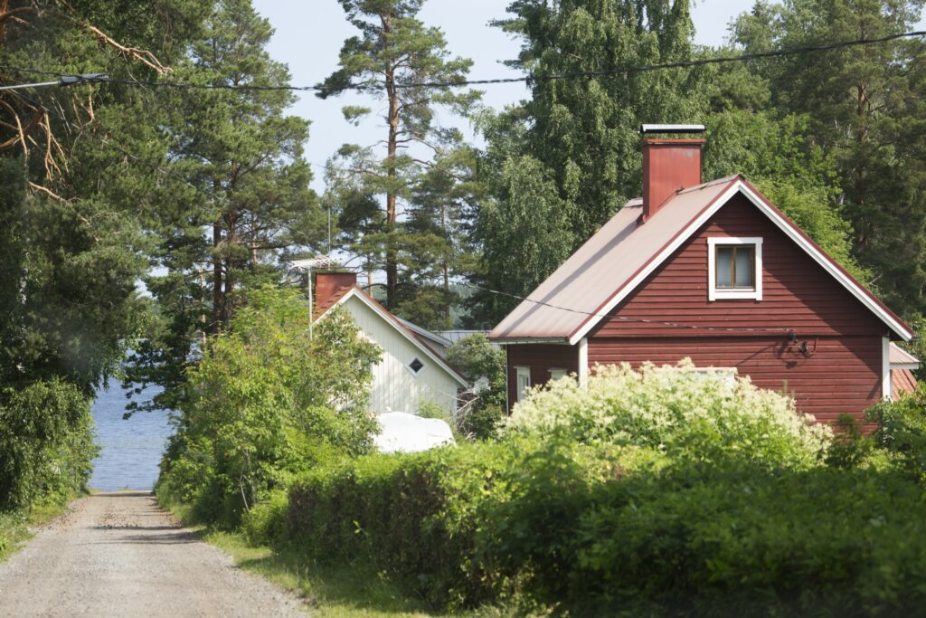 Punainen ja valkoinen puinen omakotitalo rinteessä olevalla tiellä. Taustalla kaistale järveä sekä metsää.